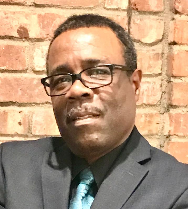 A man in a suit and tie standing next to a brick wall.